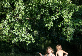 Deux enfants pagaient sur une planche gonflable sous des arbres verts à Huttopia Beaulieu sur Dordogne, France.