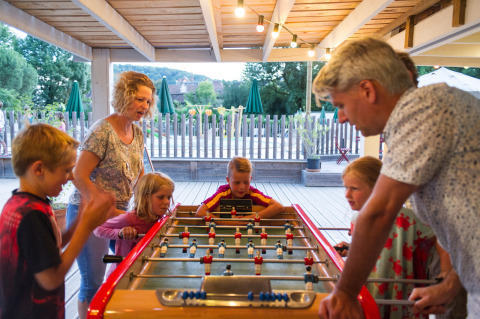 Familia jugando al futbolín bajo un porche en el parque vacacional Huttopia Beaulieu sur Dordogne, Francia.