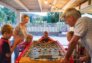 Familie spiller bordfodbold under en overdækket terrasse i ferielandsbyen Huttopia Beaulieu sur Dordogne.