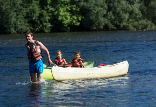 Ein Mann zieht ein Kanu mit zwei Kindern durch einen Fluss bei Beaulieu-sur-Dordogne, Occitanie, Frankreich.