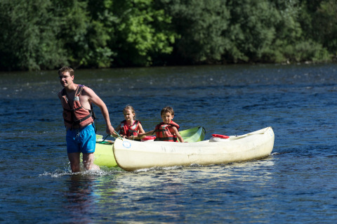 Hombre tirando de una canoa con dos niños por un río cerca de Beaulieu-sur-Dordogne, Occitania, Francia.