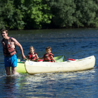 Ein Mann zieht ein Kanu mit zwei Kindern durch einen Fluss bei Beaulieu-sur-Dordogne, Occitanie, Frankreich.