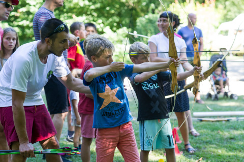 Niños aprendiendo tiro con arco al aire libre con la ayuda de un adulto en Huttopia Beaulieu sur Dordogne.