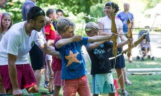 Kinder üben Bogenschießen im Freien unter Anleitung eines Erwachsenen im Huttopia Beaulieu sur Dordogne.