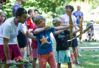 Niños aprendiendo tiro con arco al aire libre con la ayuda de un adulto en Huttopia Beaulieu sur Dordogne.