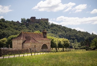 Smuk udsigt over en rustik stenbygning og grønne marker nær Huttopia Beaulieu sur Dordogne i Occitanie.