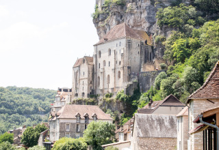 Udsigt over middelalderbygninger og klippekloster omgivet af skov nær Beaulieu-sur-Dordogne, Occitanie.