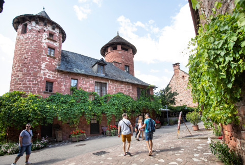 Turistas pasean por una calle empedrada junto a edificios de piedra roja cerca de Beaulieu-sur-Dordogne, Occitania.