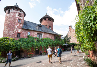 Turister slentrer gennem en malerisk, vinbedækket landsby med røde stenhuse nær Beaulieu-sur-Dordogne.