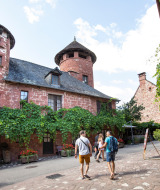 Touristen spazieren durch ein charmantes Dorf mit roten Steinhäusern in der Nähe von Beaulieu-sur-Dordogne.
