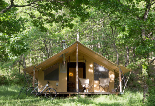 Tienda Trappeur tipo safari en Huttopia Lac de Serre Ponçon, Francia, rodeada de frondosos árboles.