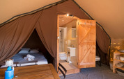 Interior de una tienda safari con cama doble, baño privado y mesa de comedor, ideal para glamping cómodo.