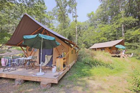 Safari-Zelte im Huttopia Lac de Serre Ponçon in Frankreich, umgeben von Wald mit Sitzbereich draußen.