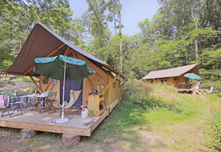 Safari-Zelte im Huttopia Lac de Serre Ponçon in Frankreich, umgeben von Wald mit Sitzbereich draußen.