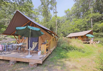 Safari-Zelte im Huttopia Lac de Serre Ponçon in Frankreich, umgeben von Wald mit Sitzbereich draußen.