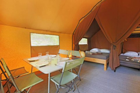 Interior de la tienda Canadienne II con mesa de comedor y camas, en Huttopia Lac de Serre Ponçon, Francia.