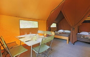 Interior de la tienda Canadienne II con mesa de comedor y camas, en Huttopia Lac de Serre Ponçon, Francia.
