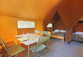 Interior de la tienda Canadienne II con mesa de comedor y camas, en Huttopia Lac de Serre Ponçon, Francia.