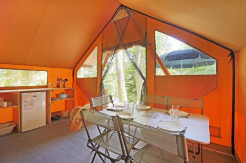Interior de una tienda safari Canadienne con mesa de comedor, sillas y cocina en Huttopia Lac de Serre Ponçon.