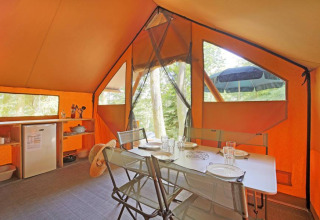 Interior de una tienda safari Canadienne con mesa de comedor, sillas y cocina en Huttopia Lac de Serre Ponçon.