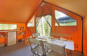Interior of a Canadienne safari tent with dining table, chairs, and kitchenette at Huttopia Lac de Serre Ponçon.