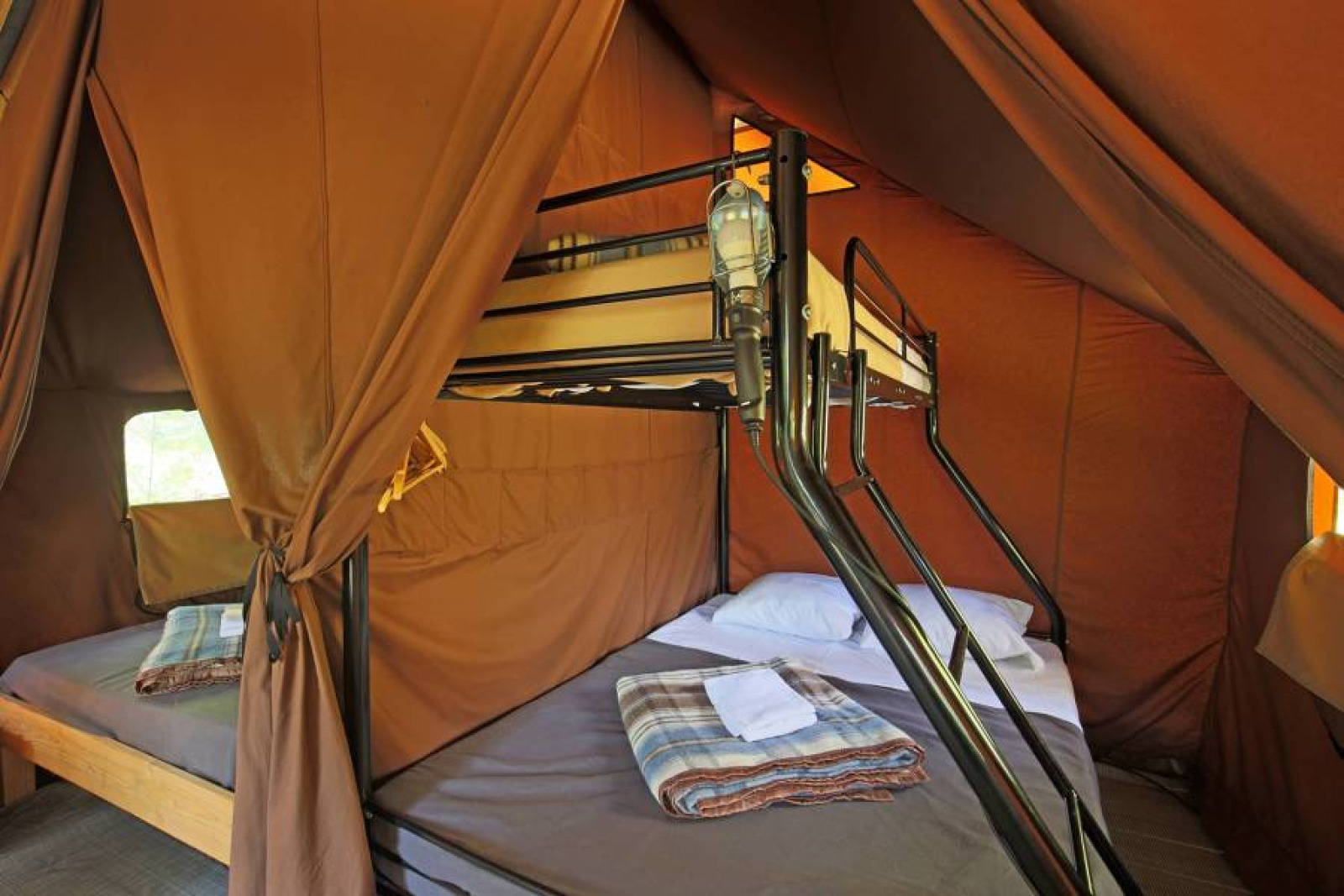 Interieur van de Canadienne Tent II met stapelbedden en dekens bij Huttopia Lac de Serre Ponçon in Frankrijk.