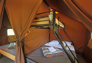 Vista interior de la Canadienne Tent II con literas y mantas en Huttopia Lac de Serre Ponçon, Francia.