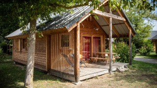 Montana chalet Vista houten huisje met veranda en picknicktafel, omgeven door bomen en groen.