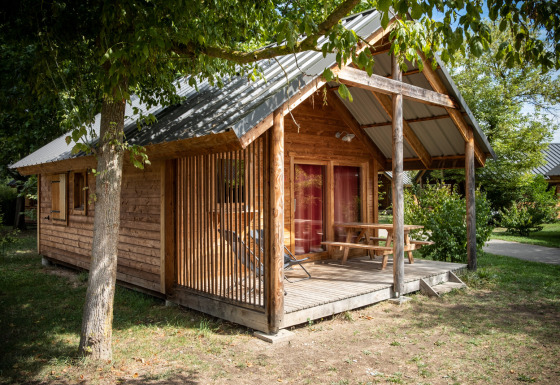 Montana chalet Vista houten huisje met veranda en picknicktafel, omgeven door bomen en groen.