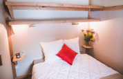 Hyggeligt soveområde i Montana chalet Vista på Huttopia Lac de Serre Ponçon, Frankrig, med blomster og lamper.
