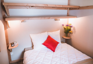 Hyggeligt soveområde i Montana chalet Vista på Huttopia Lac de Serre Ponçon, Frankrig, med blomster og lamper.