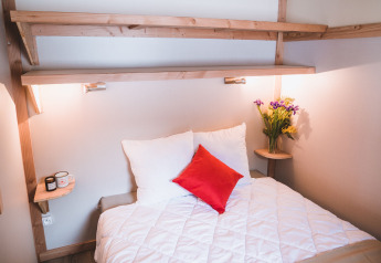 Hyggeligt soveområde i Montana chalet Vista på Huttopia Lac de Serre Ponçon, Frankrig, med blomster og lamper.