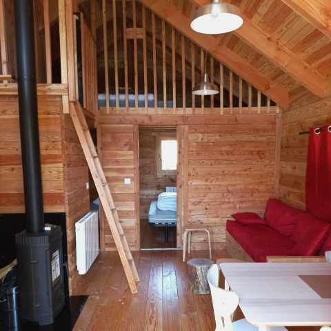 Interior de madera del chalet Montana Vista en Huttopia Lac de Serre Ponçon, sala acogedora con altillo y sofá rojo.