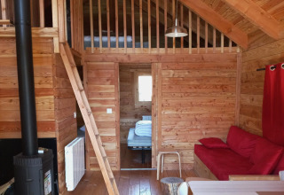Interior de madera del chalet Montana Vista en Huttopia Lac de Serre Ponçon, sala acogedora con altillo y sofá rojo.