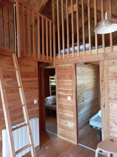 Interieur van een glampingverblijf met houten wanden, mezzanine, ladder en toegang tot slaapkamers.