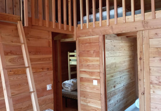 Interno di un alloggio glamping con pareti in legno, soppalco, scala e camere da letto accoglienti.