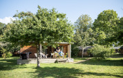 Una acogedora cabaña de madera con terraza y muebles de exterior bajo árboles en Chalet Portland, Huttopia Lac de Serre Ponçon.