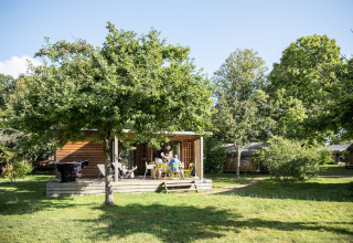 Een gezellige houten chalet met terras en tuinmeubilair onder bomen bij Chalet Portland, Huttopia Lac de Serre Ponçon.