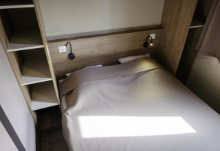 Moderne soveværelse på Chalet Portland, Huttopia Lac de Serre Ponçon, Frankrig med dobbeltseng og praktiske hylder.