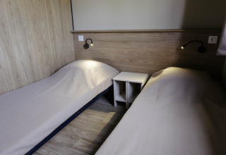 Dos camas individuales en una sencilla habitación de madera en Chalet Portland, Huttopia Lac de Serre Ponçon, Francia.