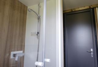 Moderne douche in Chalet Portland bij Huttopia Lac de Serre Ponçon, Frankrijk, met houten wand en grijze deur.