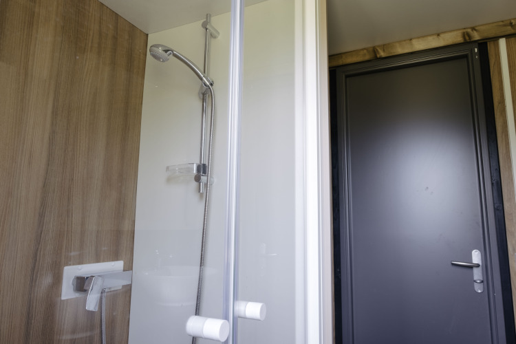 Ducha moderna en Chalet Portland, Huttopia Lac de Serre Ponçon, Francia, con pared de madera y puerta gris.