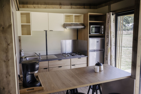 Cocina moderna en Chalet Portland de Huttopia Lac de Serre Ponçon, Francia, con estufa y refrigerador.