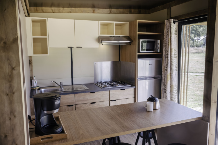 Cocina moderna en Chalet Portland de Huttopia Lac de Serre Ponçon, Francia, con estufa y refrigerador.