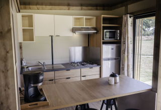 Cocina moderna en Chalet Portland de Huttopia Lac de Serre Ponçon, Francia, con estufa y refrigerador.