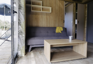 Interiør i Chalet Portland med grå sofa, træbord og udsigt til terrasse på Huttopia Lac de Serre Ponçon.
