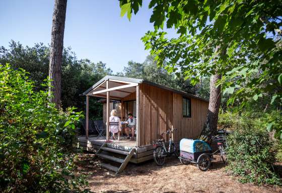 Dos personas descansan en el porche de Chalet Evasion, una cabaña de madera rodeada de naturaleza.