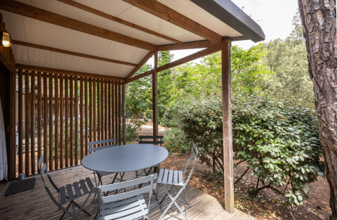 Terraza cubierta en Chalet Evasion, Huttopia Chardons Bleus - Ile de Ré, con mesa, sillas y vegetación.