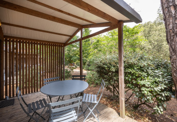Udendørs terrasse ved Chalet Evasion, Huttopia Chardons Bleus - Ile de Ré, med bord, stole og grøn beplantning.