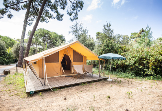 Safari bungalowtelt Classic på Huttopia Chardons Bleus - Ile de Ré med veranda og solparasol i naturen.